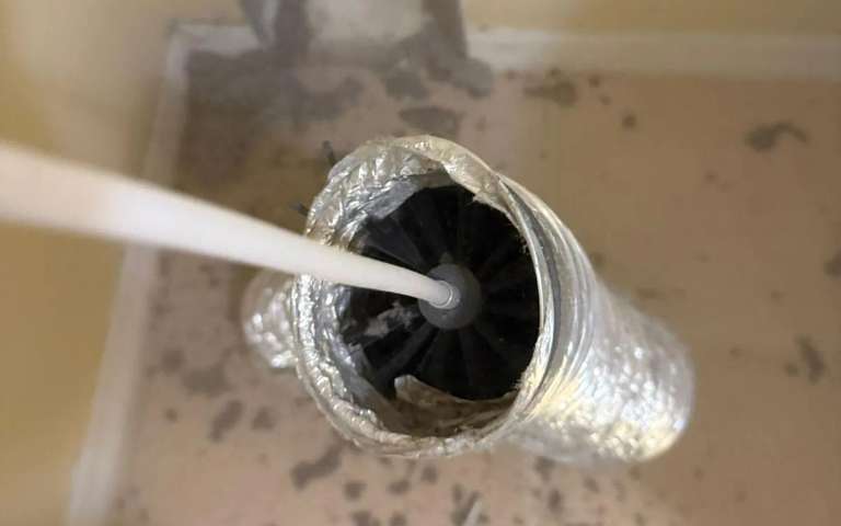 A spinning brush head inside a flexible foil duct with lint on the floor around it