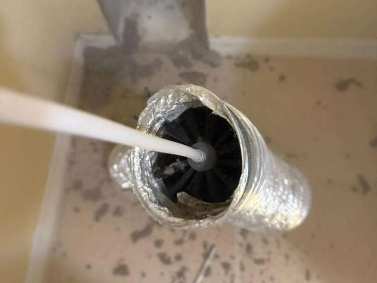 A spinning brush head inside a flexible foil duct with lint on the floor around it