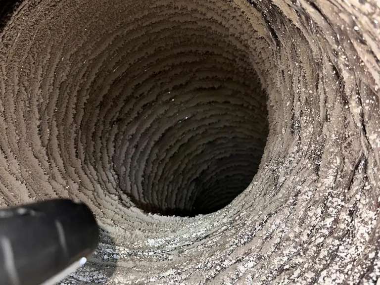 The inside of a flexible duct coated in packed lint, a drill-driven brush entering at the left