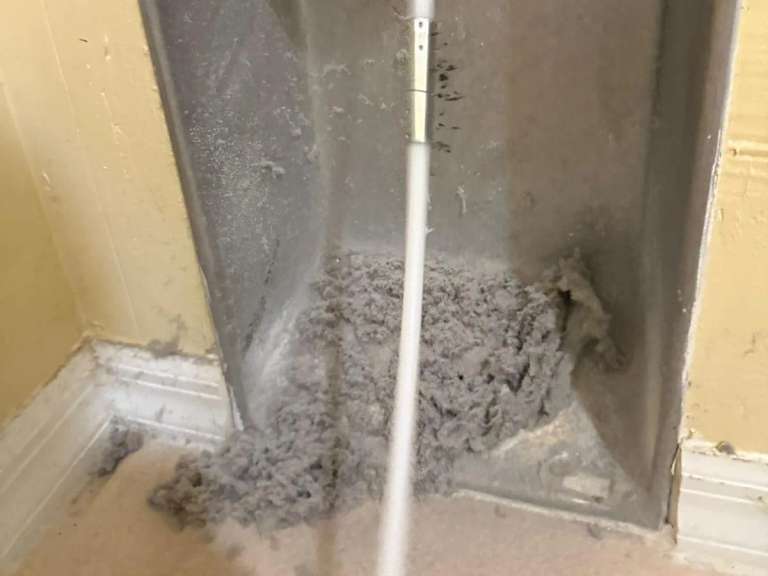 A rod and a pile of lint at a recessed dryer wall box
