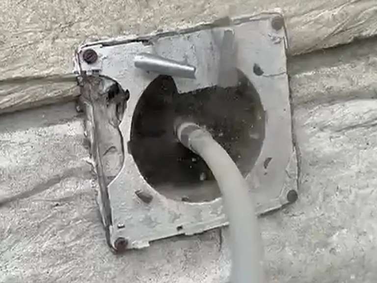 A hose or brush feeding into an exterior vent opening on a stucco wall